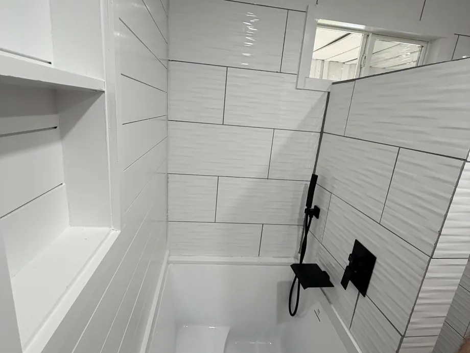 Remodeled bathroom with a white tiled shower, built-in shelves and black fixtures